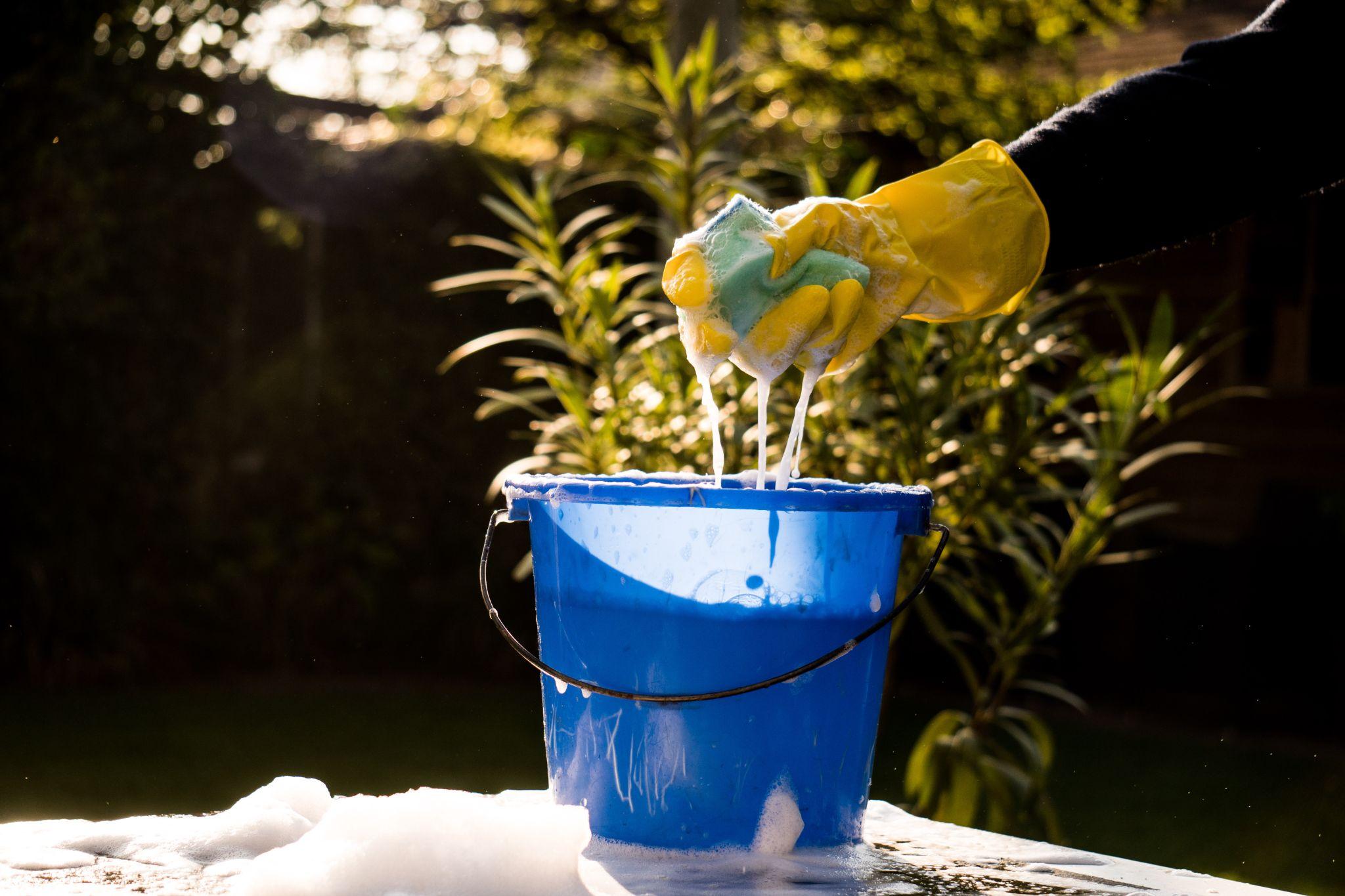 Spring Cleaning outside with big yellow cleaning gloves, water, soap and a big blue bucket with soap.