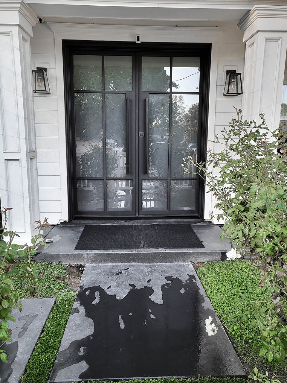 Image of a dark-finished custom iron door with an intricate design attached to a white home